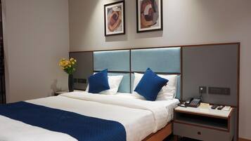 A hotel room with a large bed, a nightstand with a phone and a lamp, and two framed artworks on the wall.