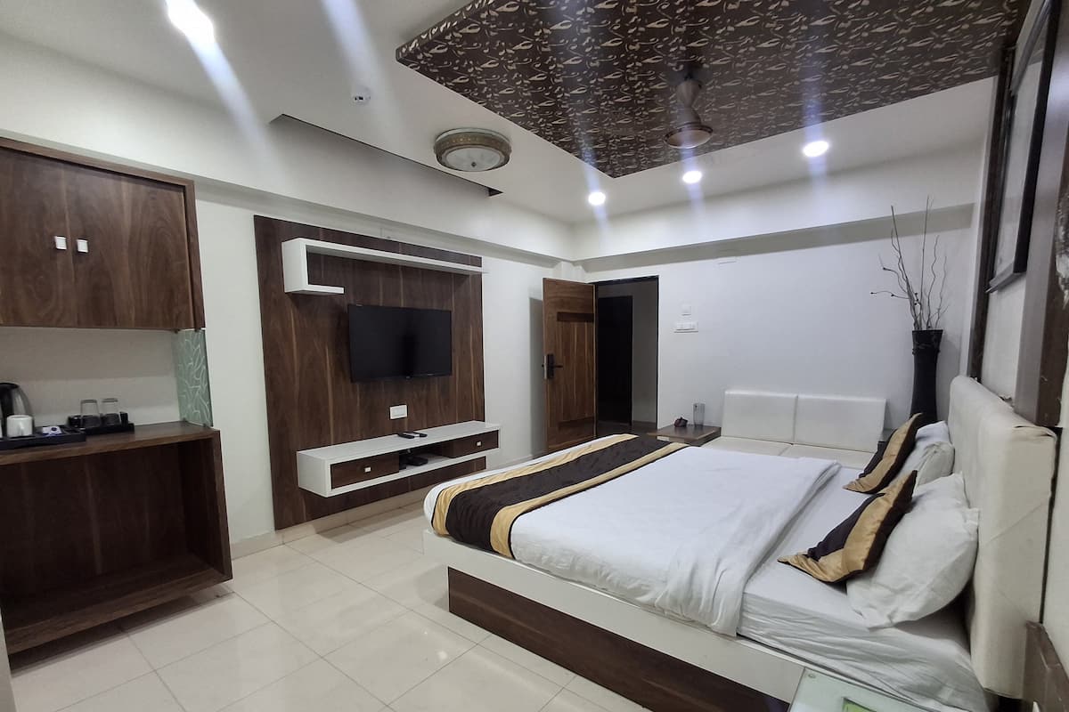 Een moderne slaapkamer met een groot bed, een aan de muur bevestigde televisie en een nachtkastje met een lamp.
