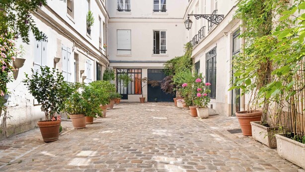 Un patio empedrado con macetas y un edificio con puerta negra.