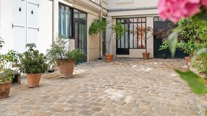 Un patio con suelo de adoquines, plantas en macetas y un edificio con ventanas y puertas grandes.