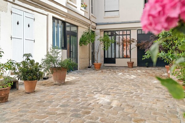 A courtyard with cobblestone flooring, potted plants, and a building with large windows and doors.