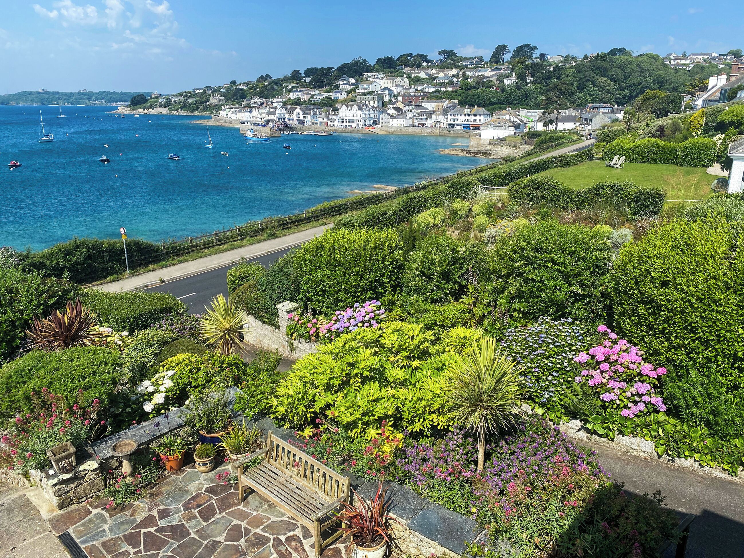 A coastal town with a stone pathway leading to a bench overlooking a sea view.
