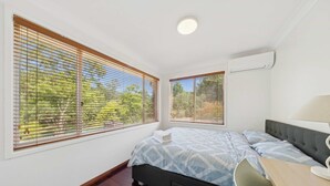 A bedroom with a bed, a desk, and two windows with blinds.