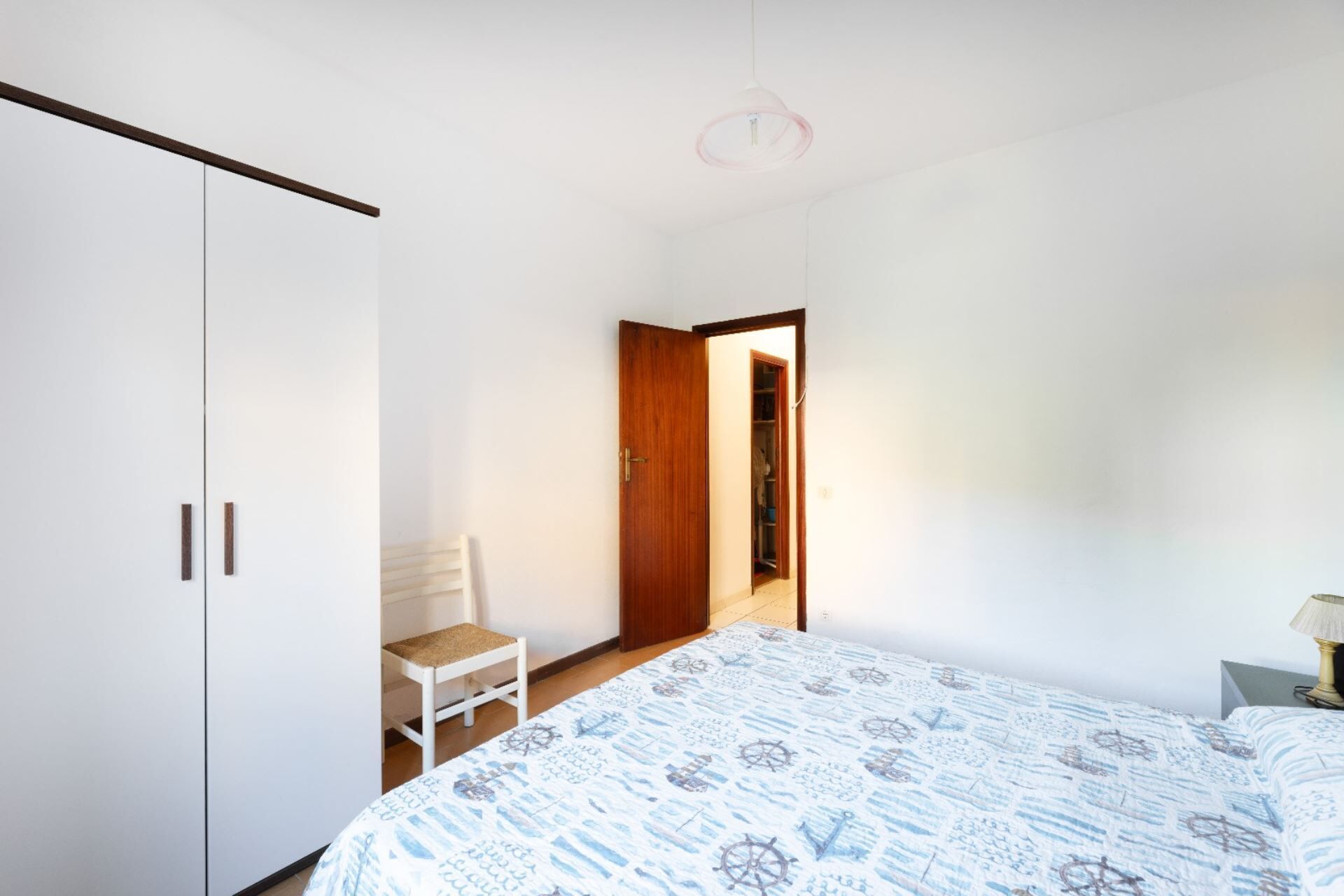 A bedroom with a bed, a chair, a wardrobe, and a door leading to another room.