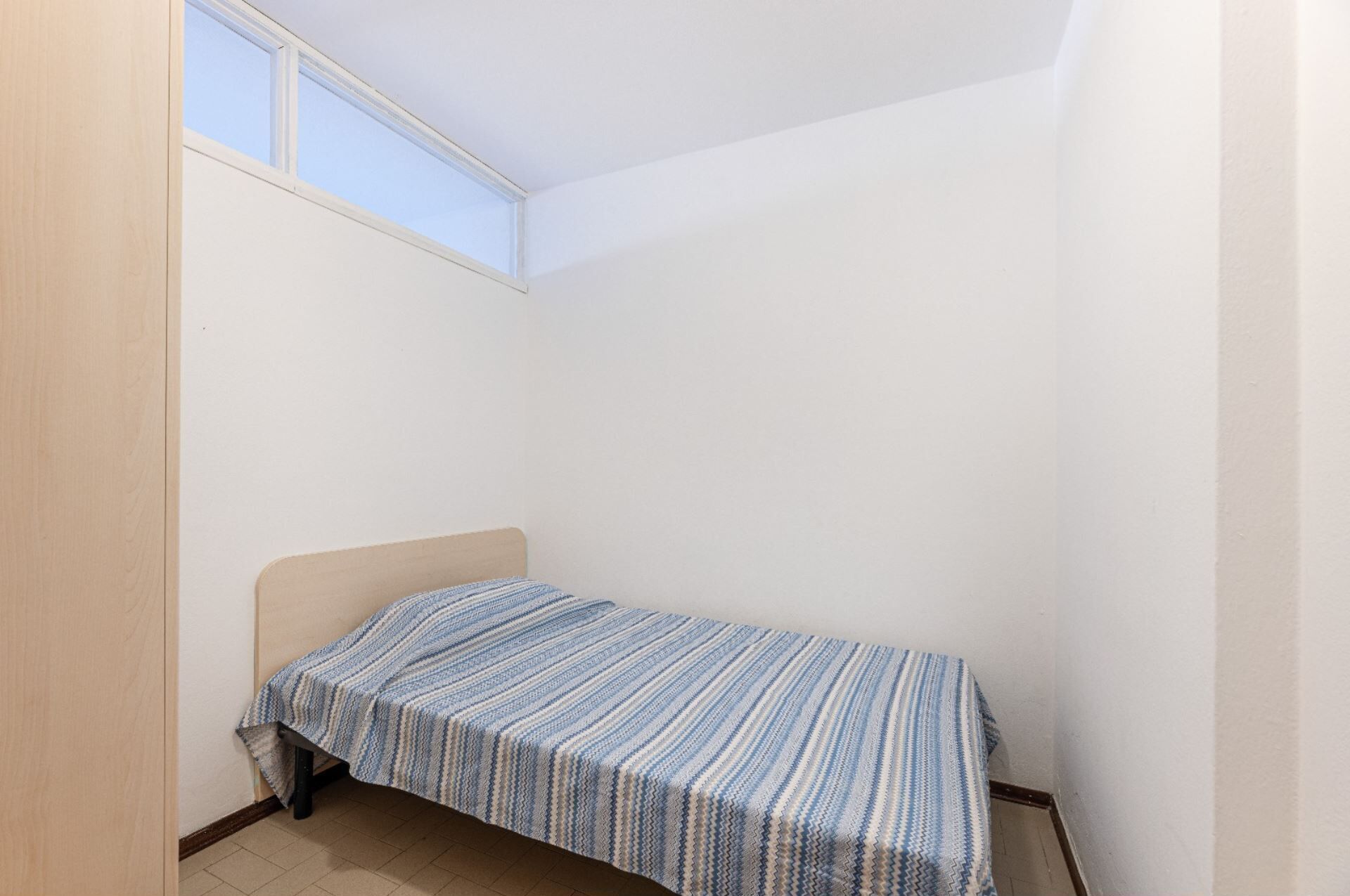 A small, single-bed room with a sloped ceiling and a window.