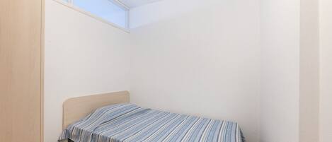 A small, single-bed room with a sloped ceiling and a window.