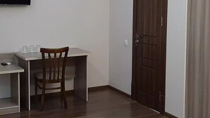 A small room with a wooden desk, a chair, a television mounted on the wall, and a wooden door. - Grand Vizir hotel (Khiva)