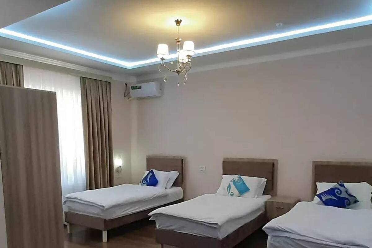 Camera d'albergo con tre letti singoli, un lampadario e una fascia di luci a soffitto.