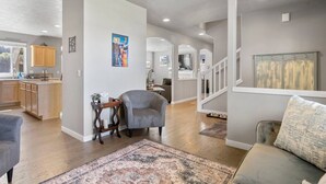 A spacious living area with a grey armchair, a patterned rug, and a kitchen in the background. - Fantastic High Desert Retreat, Pet Friendly, Fenced Backyard w/ Covered Patio, Ping Pong, BBQ (Bend)