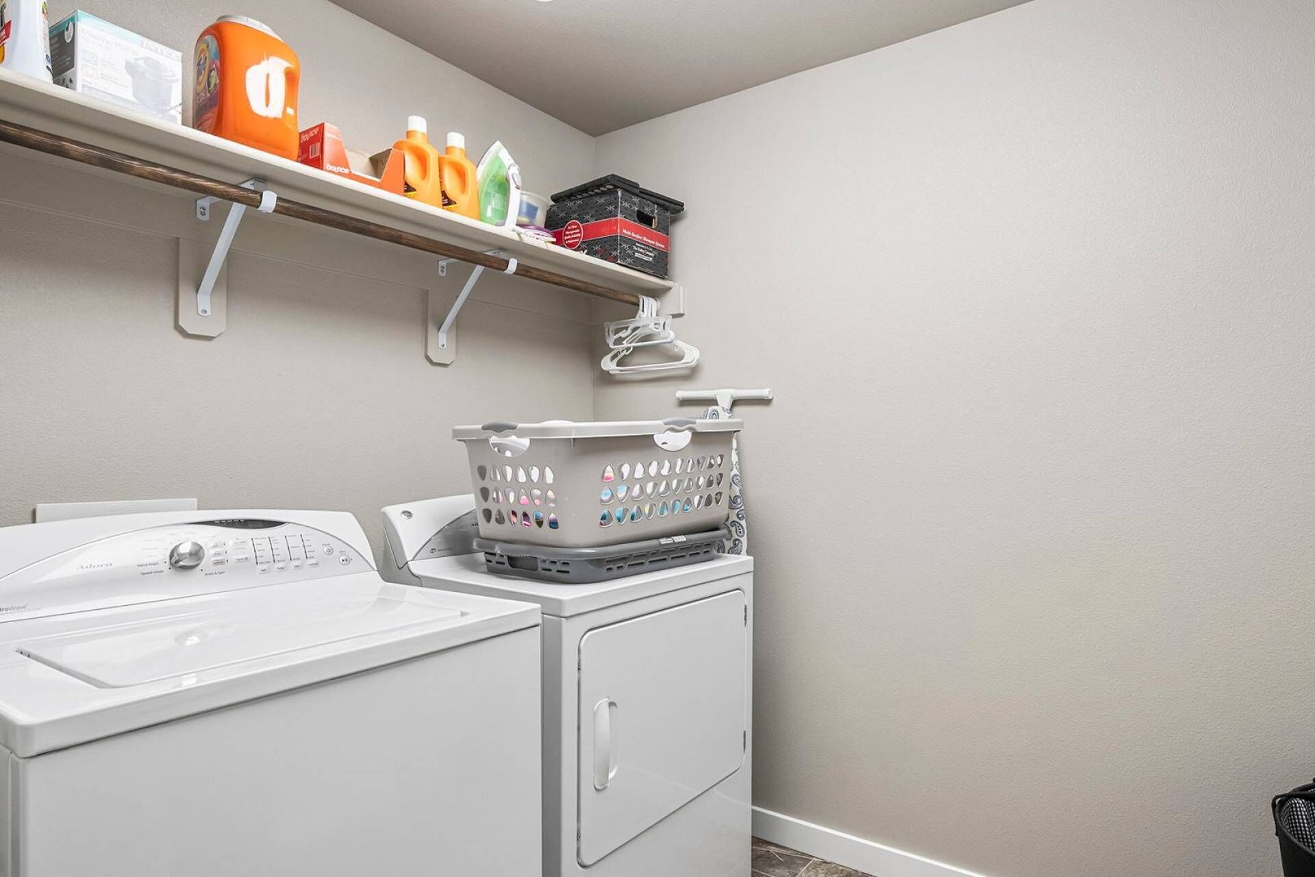 A laundry area with a washing machine, a dryer, and shelves above holding cleaning supplies.