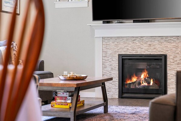 A living room with a fireplace, a television mounted above it, and a table with DVDs.