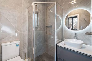 Une salle de bain moderne avec une douche à parois de verre, un miroir rond et un lavabo blanc.
