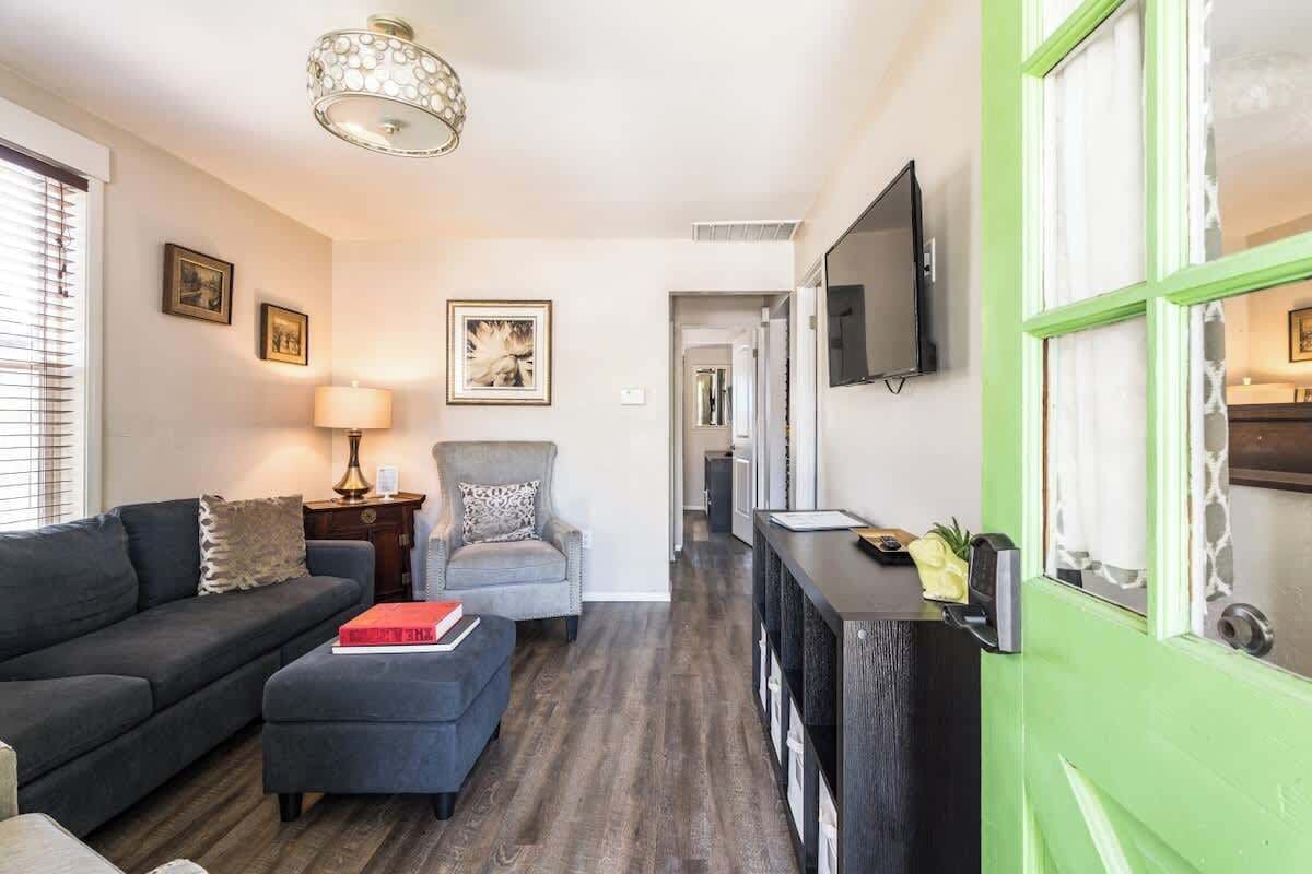 En moderne stue med sofa, lænestol, sk footstool og et tv ophængt på væggen.