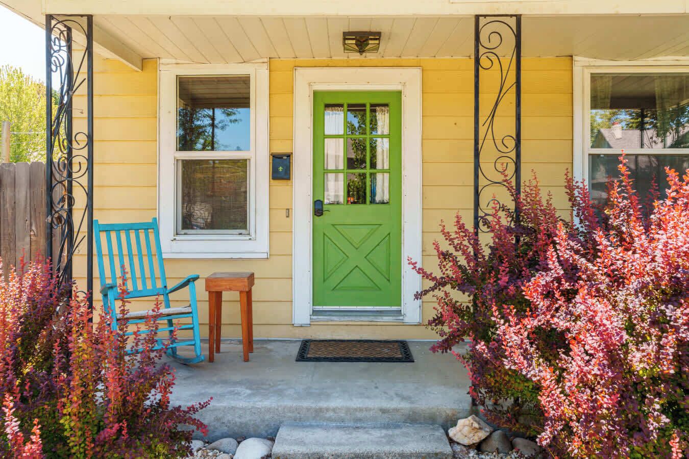 Een huis met een groene deur, een blauwe stoel en een kleine tafel op de veranda.