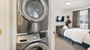 Une chambre d’hôtel équipée d’un lave-linge et d’un sèche-linge intégrés, d’un lit, d’une télévision et d’une fenêtre avec des rideaux.