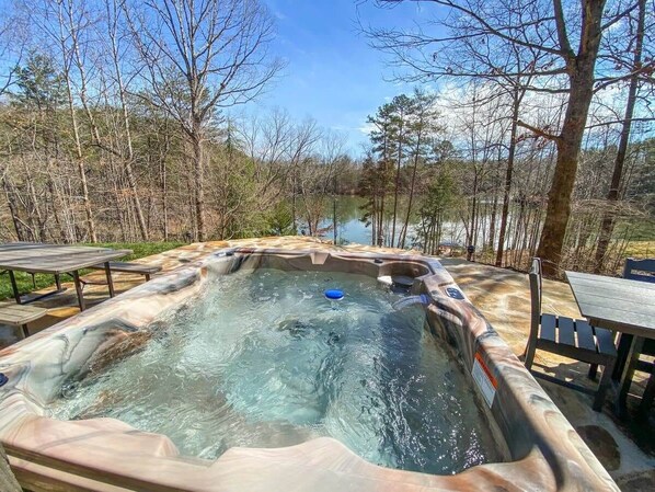 Un jacuzzi rodeado por un paisaje natural con árboles y una masa de agua al fondo.