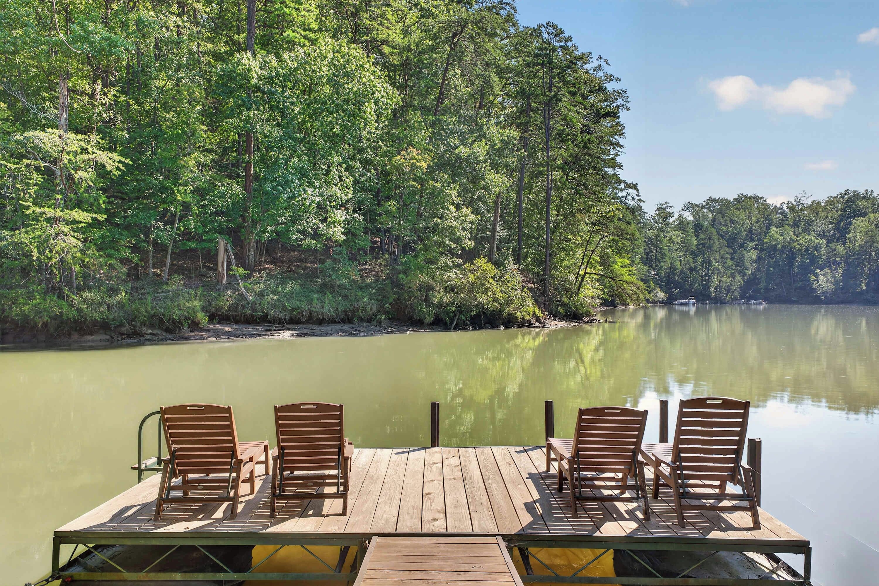 Une jetée en bois, avec quatre chaises en bois disposées face à un lac paisible, le tout entouré d’une forêt dense.