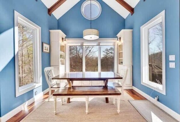 A dining room with a large table and chairs, white cabinetry, and large windows.