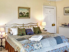 A neatly made bed with a floral quilt, a framed painting above it, and a white door to the right. - The Annex at Mains House (Tain)