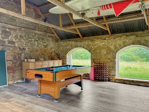 A pool table in a room with stone walls and wooden beams, large windows with a view of greenery, and a wooden cabinet. - The Annex at Mains House (Tain)