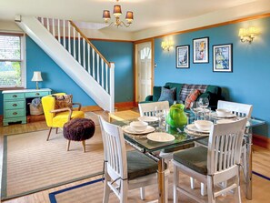 A dining area with a glass table set for six, surrounded by white chairs. A staircase with white railings leads to another room. - The Annex at Mains House (Tain)