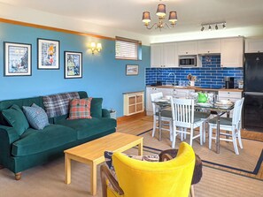 A living room with a green sofa, yellow chair, and a dining area with a table and chairs. - The Annex at Mains House (Tain)