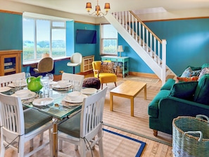 A dining area with a glass table set for four, white chairs, a green pitcher, and a television mounted on the wall. - The Annex at Mains House (Tain)