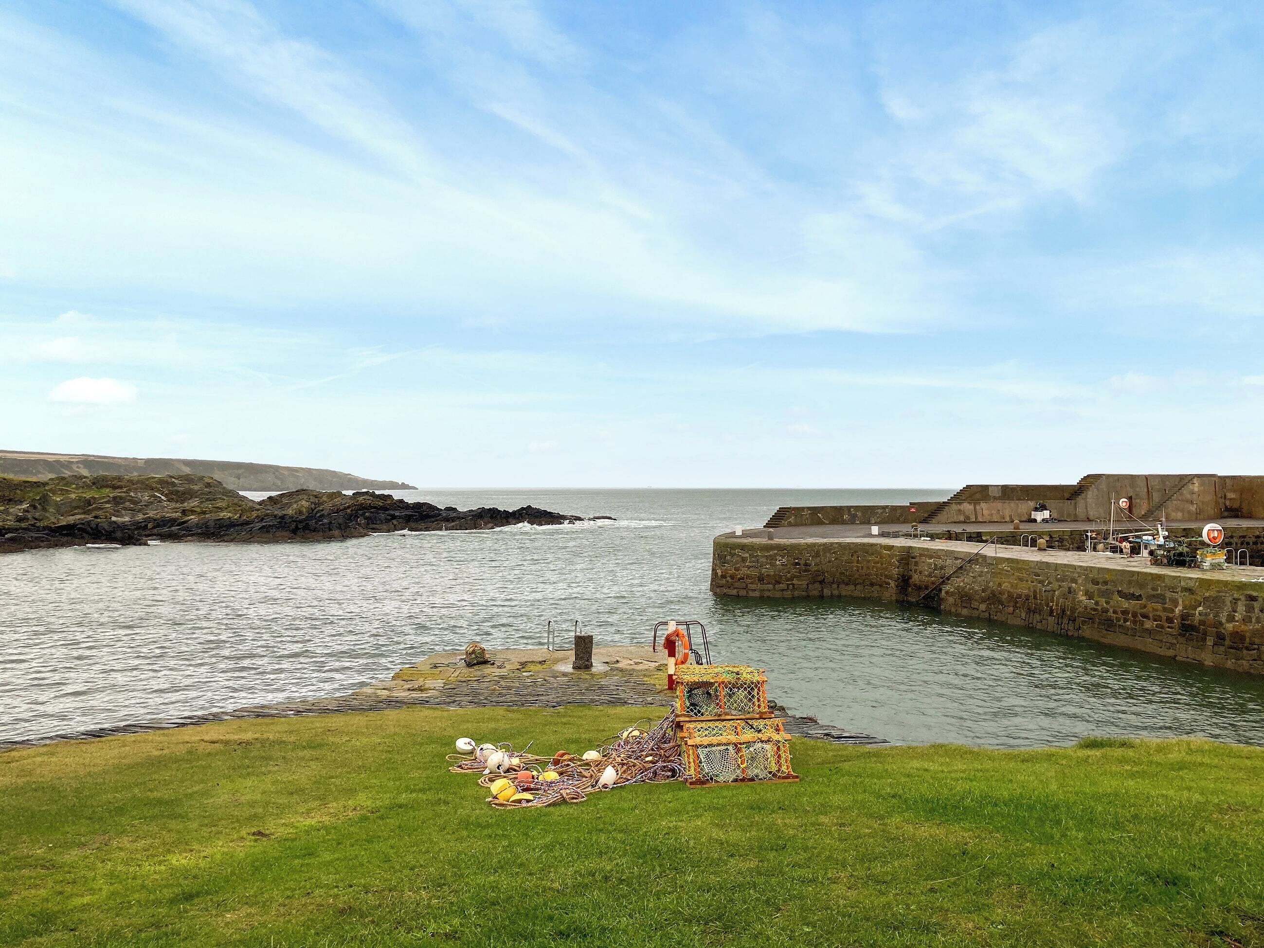 Eine Küstenlandschaft mit einer Rasenfläche, einem Steinsteg und Blick aufs Meer.