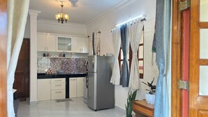 A modern kitchen with white cabinets, a black countertop, and a stainless steel refrigerator. There is a chandelier hanging from the ceiling and a potted plant on the counter. - 1bhk flat with pool view 5 mins walk to Candolim beach in a prime location. (Calangute)