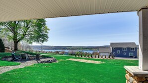 A backyard with a wooden deck, a stone wall, and a view of a lake and distant hills. - Home w/ Lake Views on Finger Lakes Wine Trail (Penn Yan)