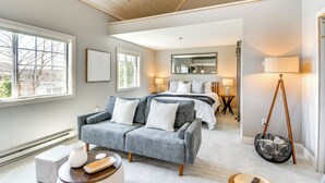 A modern hotel room with a grey sofa, a large bed, a hanging chair, and a view of the outdoors. - Home w/ Lake Views on Finger Lakes Wine Trail (Penn Yan)