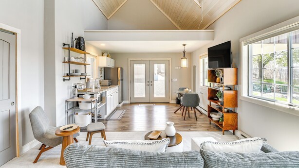 A spacious living area with a high ceiling, a kitchen with open shelving, and a dining area with a table and chairs. - Home w/ Lake Views on Finger Lakes Wine Trail (Penn Yan)