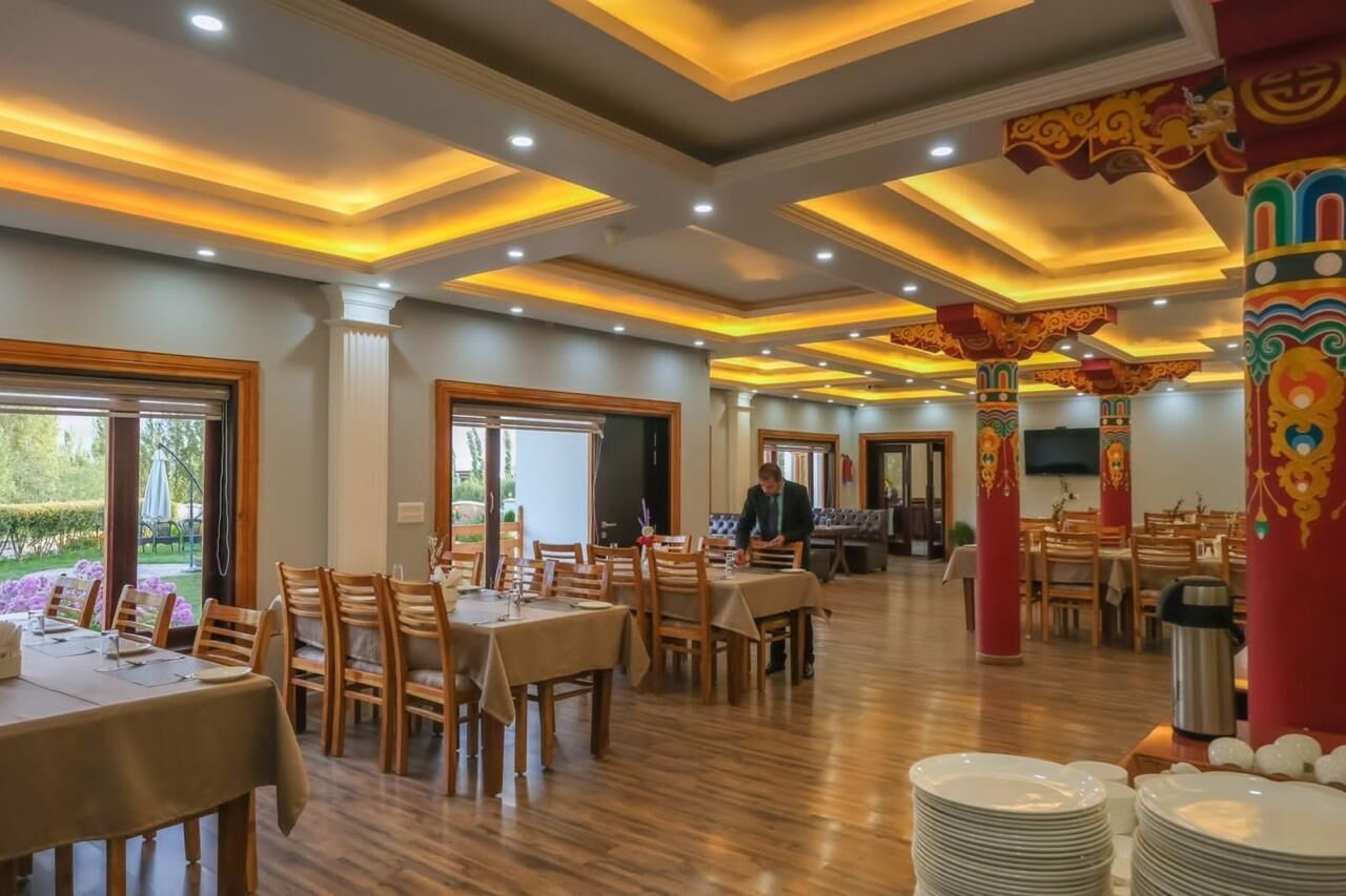 A spacious dining area with wooden tables and chairs, a central column with intricate designs, and a view of the outdoors through large windows.