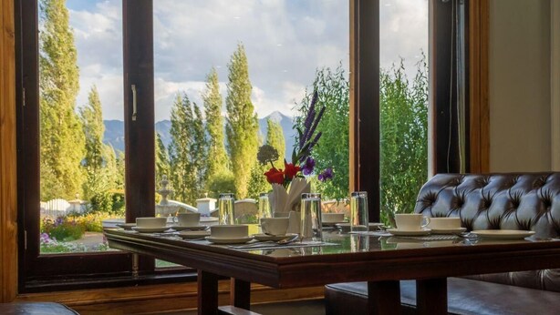 Comedor con mesa para dos, banca acolchada y vistas a un paisaje montañoso a través de amplios ventanales.