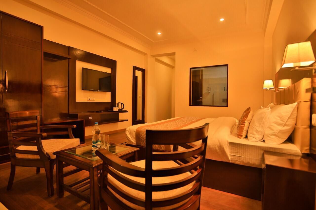 A hotel room with a bed, a desk, a chair, a TV, and a lamp.