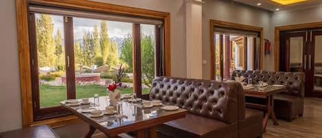 Un'area pranzo con una grande finestra, un tavolo in legno apparecchiato per quattro persone e una panca in pelle marrone.