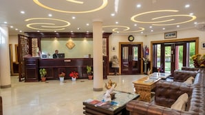Vestíbulo de hotel con mostrador de recepción, una zona de estar con sofá y un elemento decorativo central.