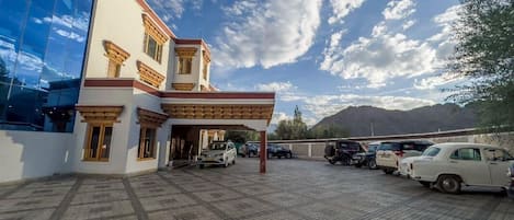 Uma área de estacionamento com vários carros, um edifício com fachada de vidro moderna e montanhas ao fundo.
