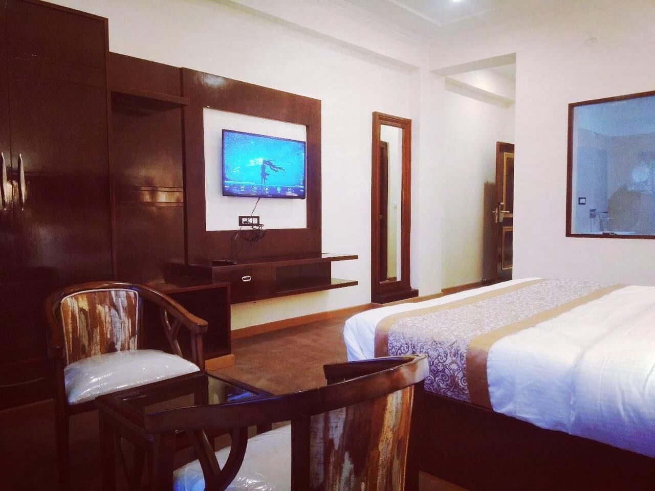 A hotel room with a bed, a desk with a chair, a television, and a mirror.
