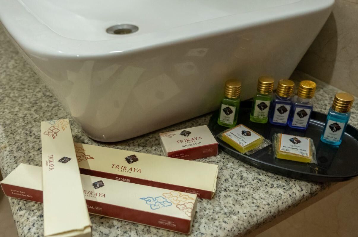A bathroom with a white bathtub, a black tray holding various toiletries, and three TRIKAYA branded shower caps and a hand soap.
