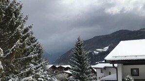 Ett snötäckt landskap med ett berg i bakgrunden, en stig som leder till en byggnad med ett snötäckt tak och snötyngda träd.