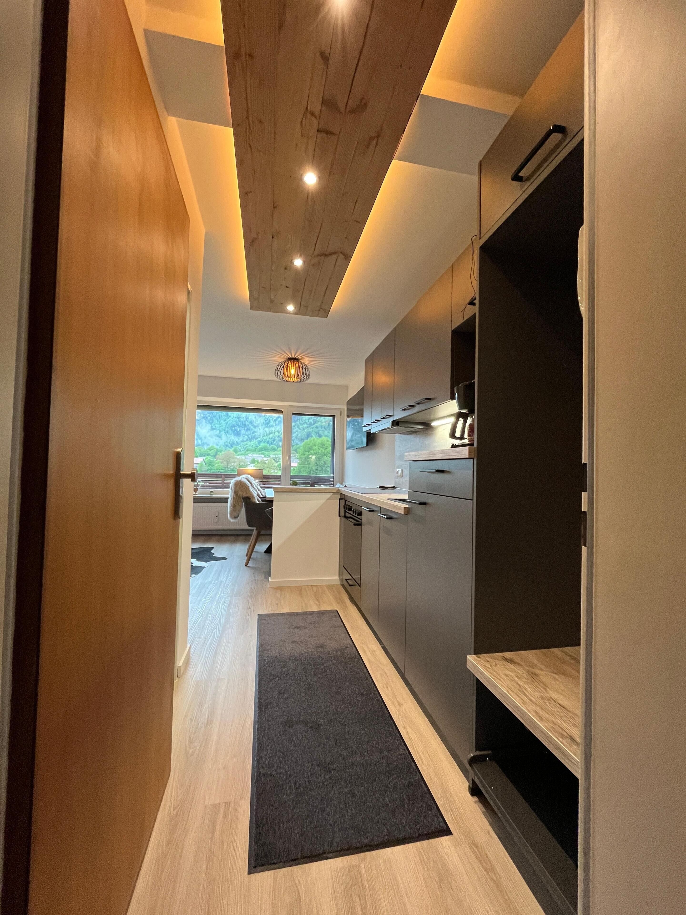 A modern kitchen with wooden ceiling beams, built-in appliances, and a view to the outdoors.