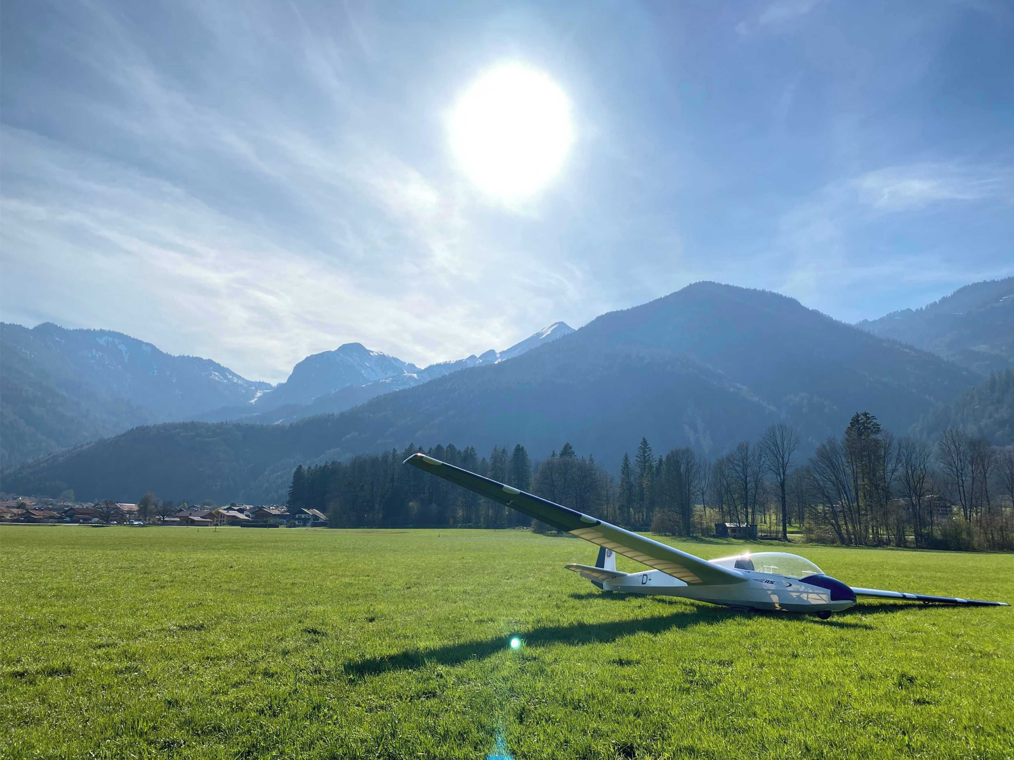 A glider on a grassy field with mountains in the background.