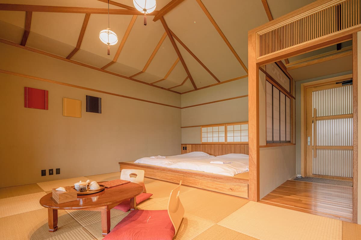 Une pièce de style japonais traditionnel, avec un sol recouvert de tatamis, un lit en bois, une petite table avec un service à thé et des portes coulissantes.