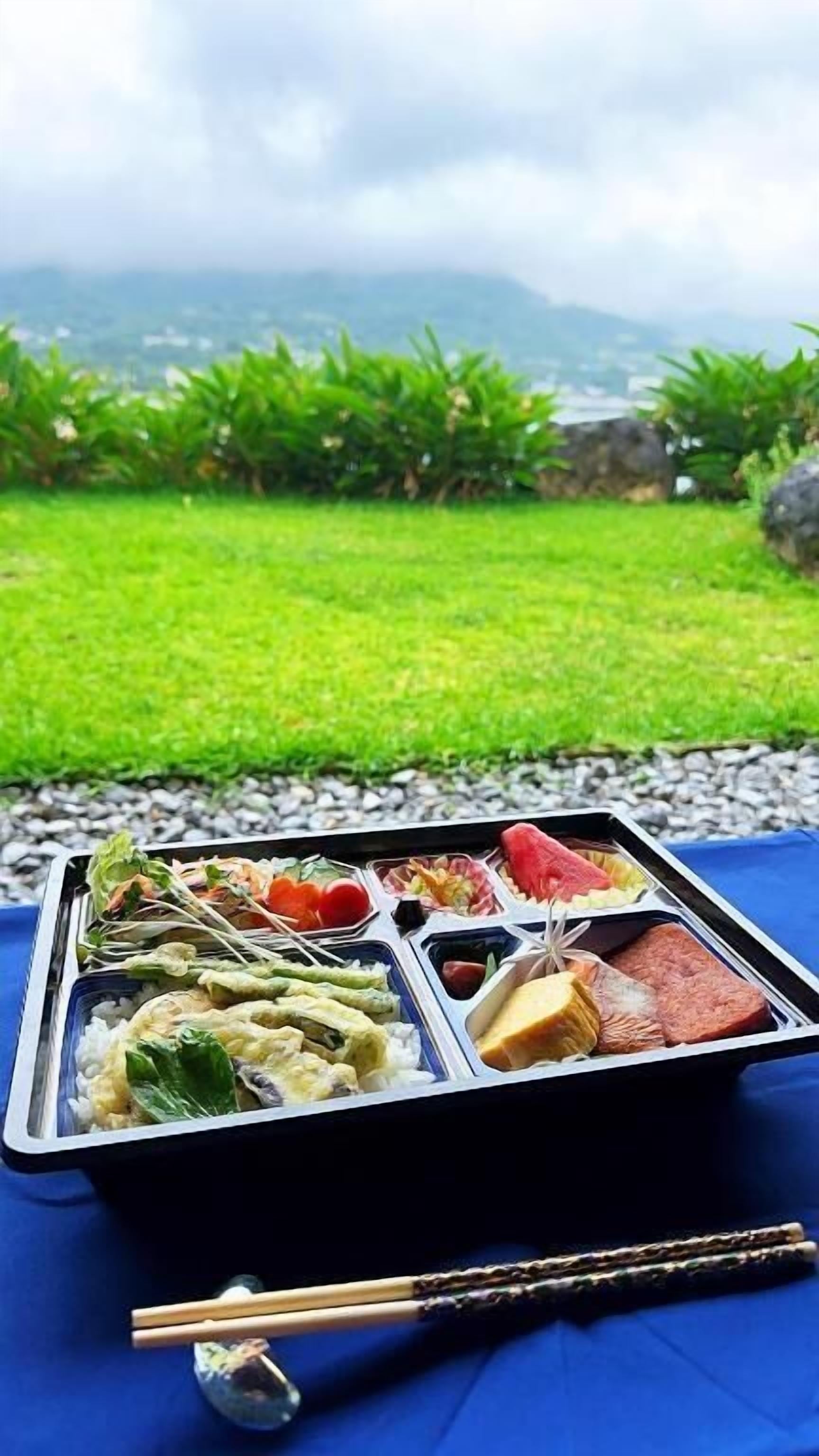 A bento box with various food items on a table outdoors.
