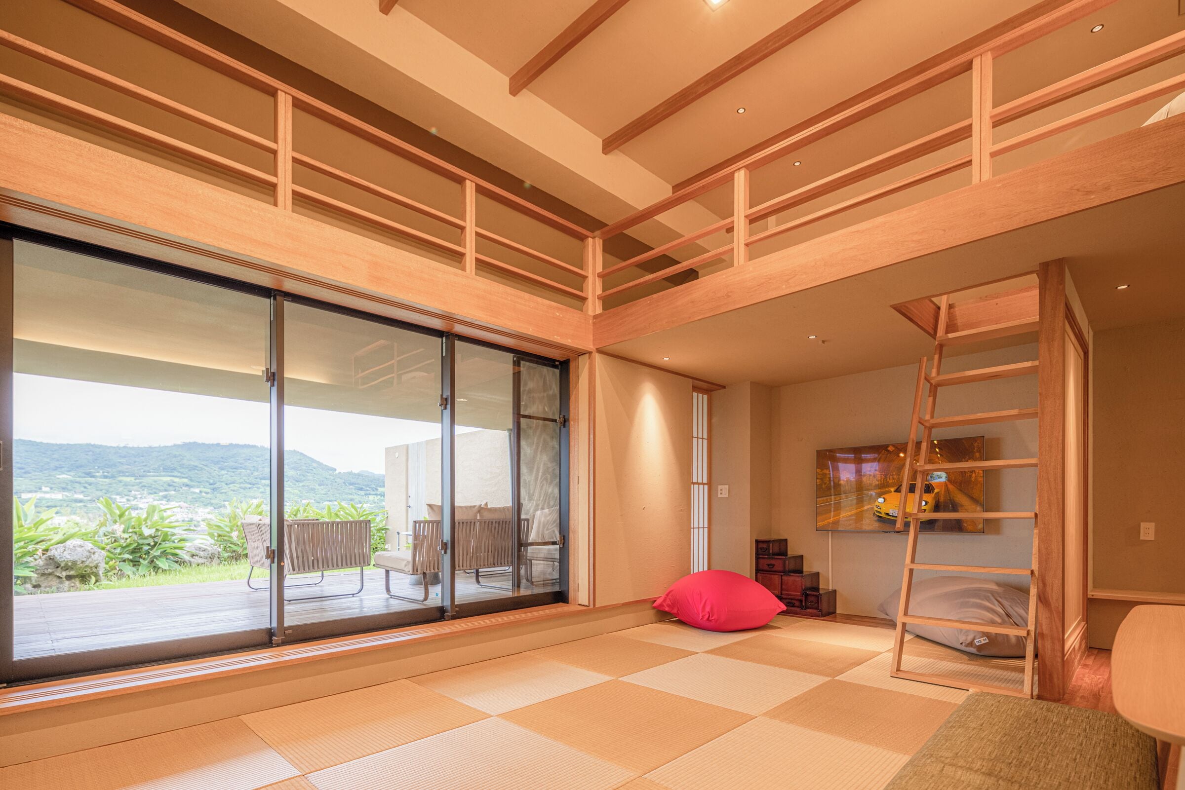 A spacious room with tatami flooring, a sliding glass door leading to a balcony, and a wooden ladder.