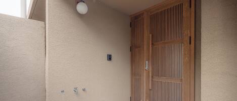 A building exterior with a beige wall, a wooden door, and a light fixture.