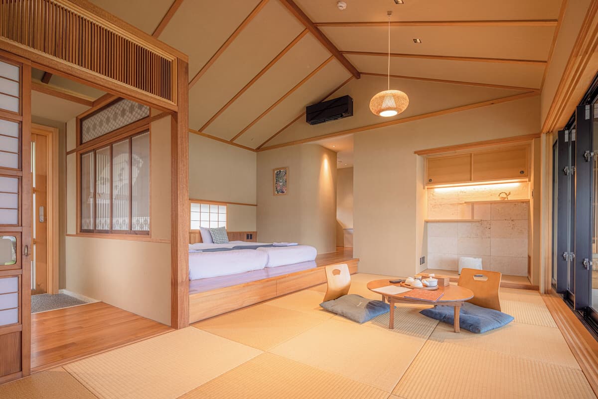 Une pièce de style japonais traditionnel, avec un sol recouvert de tatamis, un lit bas en bois, une petite table avec un service à thé et des portes coulissantes.