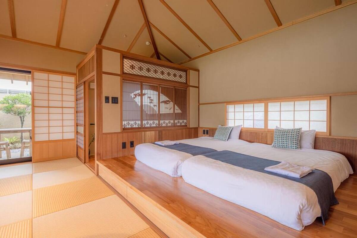 Une pièce de style japonais traditionnel, avec un sol recouvert de tatamis, un grand lit doté de nombreux oreillers et une porte coulissante agrémentée d’un paravent décoratif.