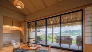 A traditional Japanese-style room with tatami flooring, a low table with cushions, and a view of a mountainous landscape through large sliding doors.